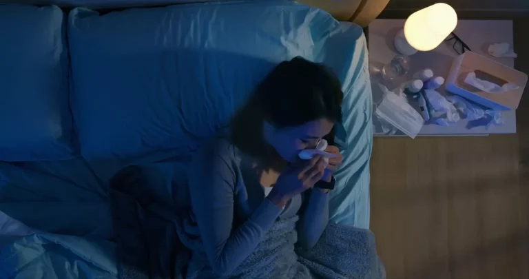 woman on her bed blowing her nose into a tissue