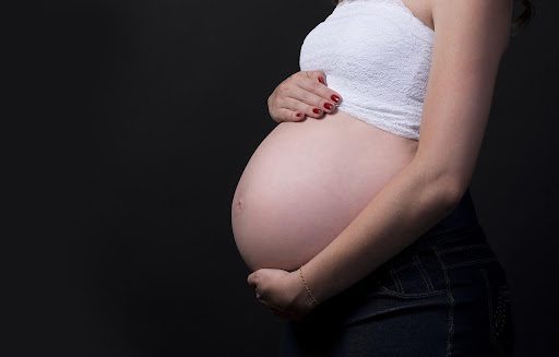 Pregnant woman holding belly standing in front of black background